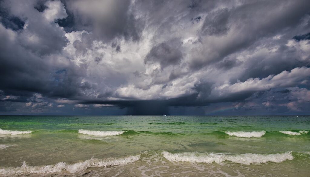 A storm with a rainbow on the Gulf of Mexico with a boat going by and the surf in the foreground.