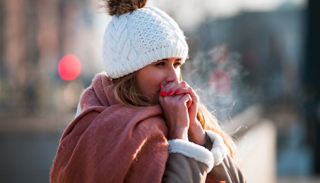 Woman breathing on her hands to keep them warm at cold winter day