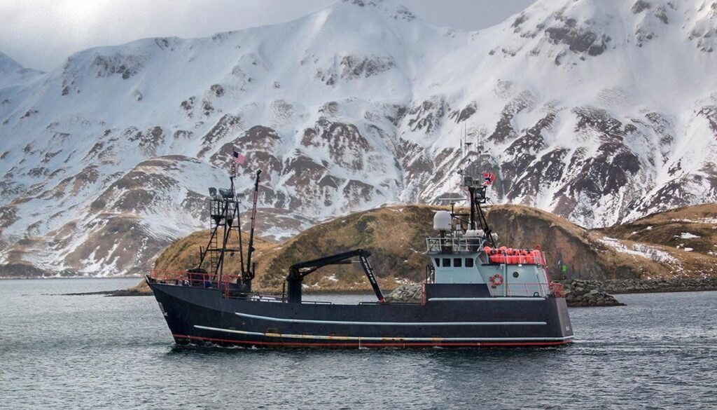 Commercial crab boat traveling with snowy mountainous background in Alaska